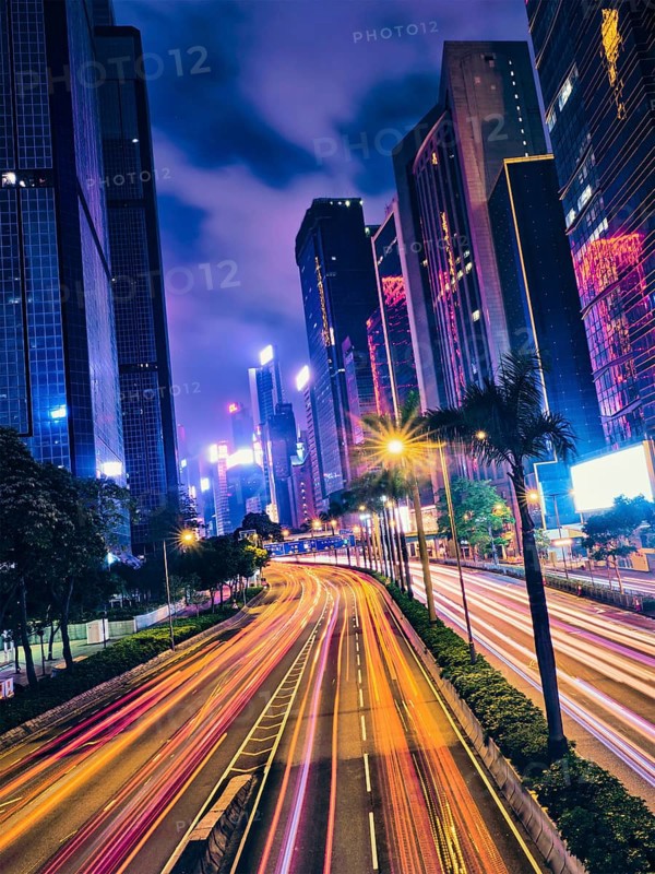 Street traffic in Hong Kong at night. Office skyscraper buildings and busy traffic on highway road with blurred cars light trails. Hong Kong