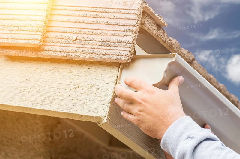 Worker attaching aluminum rain gutter to fascia of house