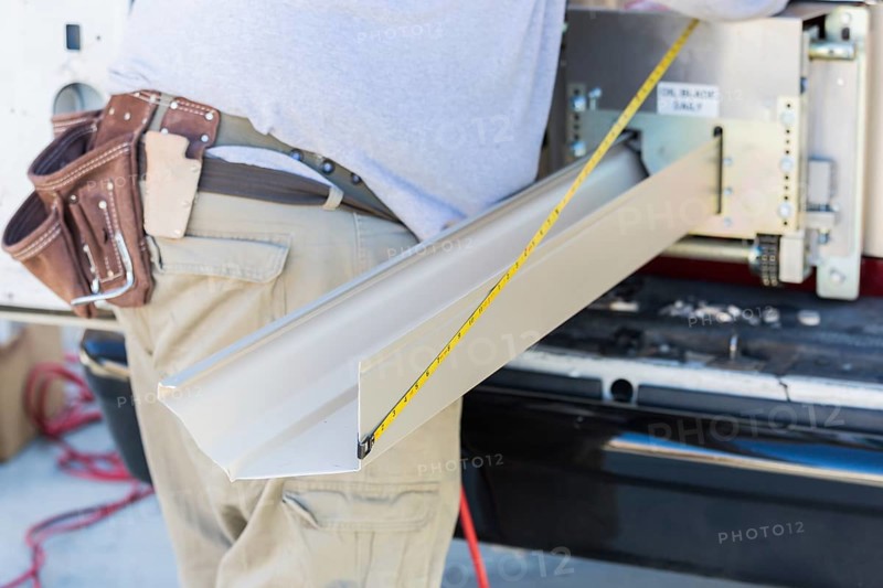 Worker measuring an aluminum rain gutter feeding through seamless shaping machine