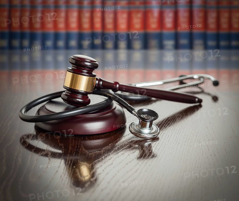 Gavel and stethoscope on wooden table with law books in background