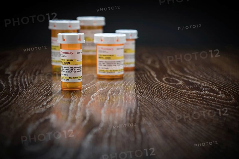 Variety of non-proprietary prescription medicine bottles on reflective wooden surface