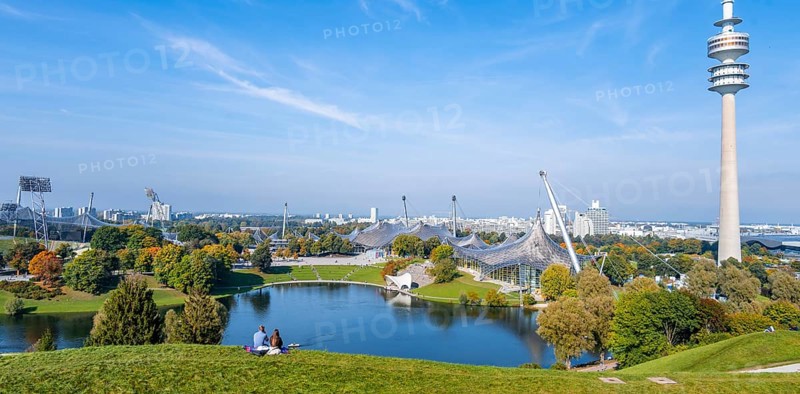 Two people sitting in the park with Olympic lake and Olympic tower