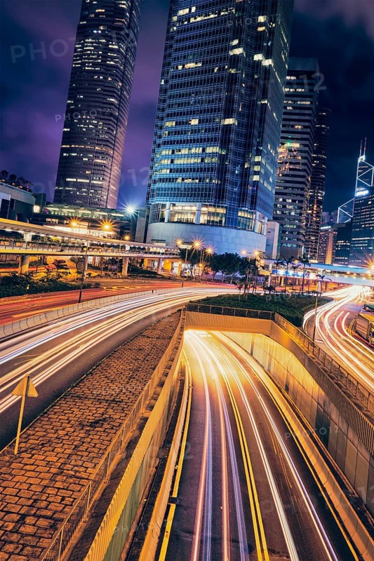 Street traffic in Hong Kong at night. Office skyscraper buildings and busy traffic on highway road with blurred cars light trails. Hong Kong