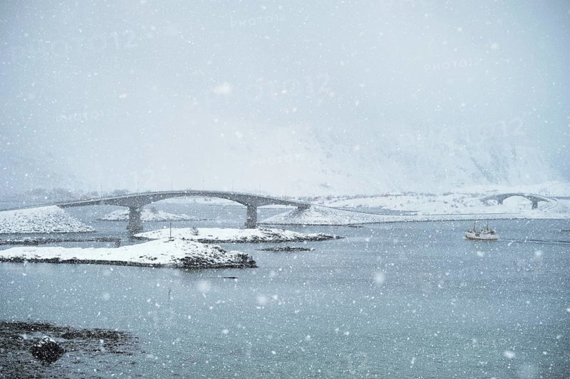 Fredvang bridges in heavy snowfall in winter with fishing ship. Lofoten islands