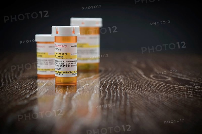 Variety of non-proprietary prescription medicine bottles on reflective wooden surface