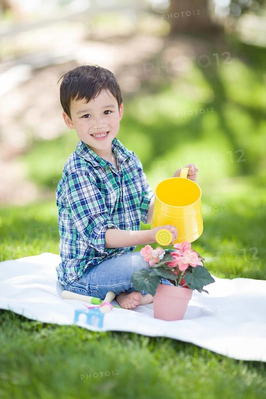mixed-race young boy watering his potted flowers outside on the grass
