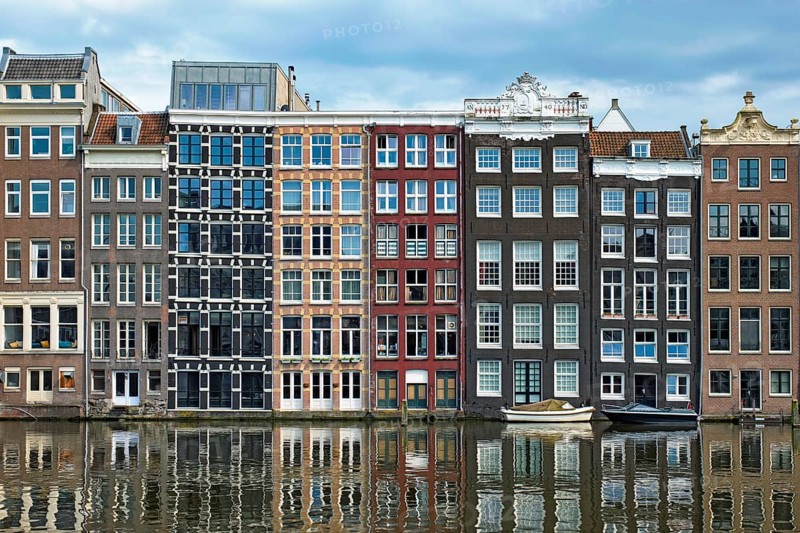 Row of typical houses and boat on Amsterdam canal Damrak with reflection. Amsterdam