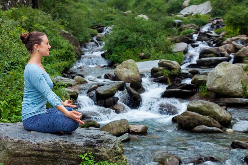 Woman in Hatha yoga asana Padmasana outdoors at tropical waterfall