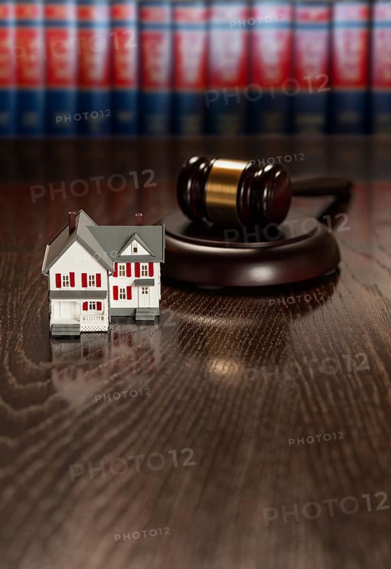 Gavel and small model house on wooden table with law books in background