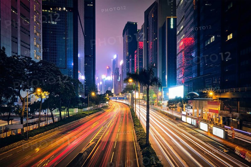 Street traffic in Hong Kong at night. Office skyscraper buildings and busy traffic on highway road with blurred cars light trails. Hong Kong