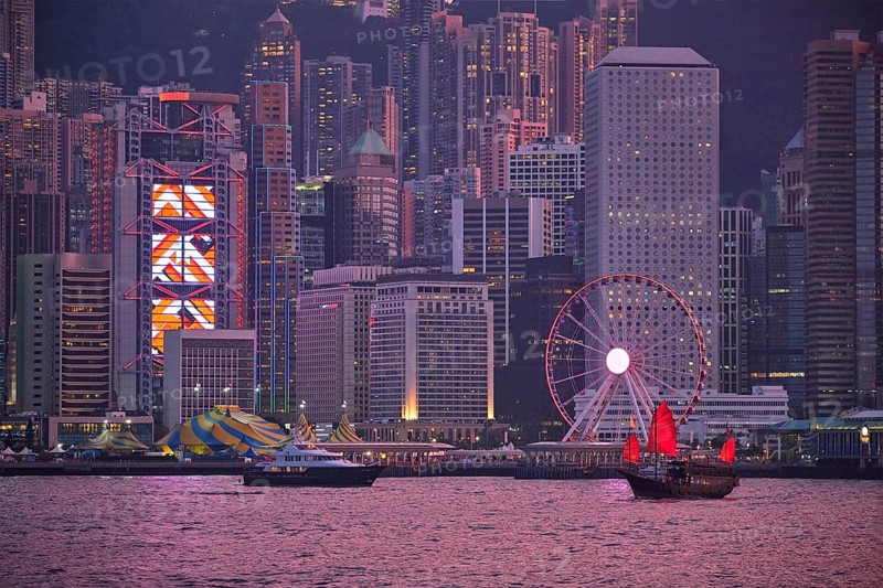 Tourist junk boat ferry with red sails and Hong Kong skyline cityscape downtown skyscrapers over Victoria Harbour in the evening. Hong Kong