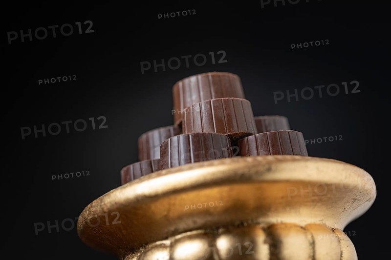 Stack of fine chocolates on golden pillar dish with dark background