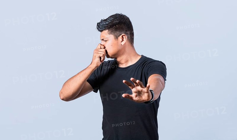 Confused unhappy man grabbing nose with fingers and stretching hand out feeling disgusted