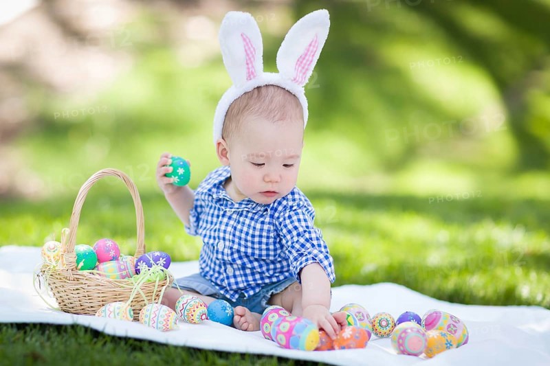 mixed-race chinese and caucasian baby boy outside wearing rabbit ears playing with easter eggs