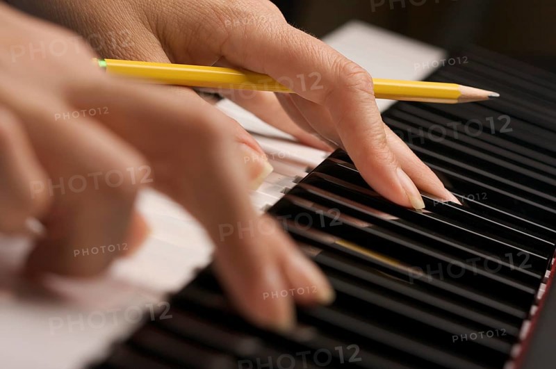 Woman's fingers with pencil on digital piano keys