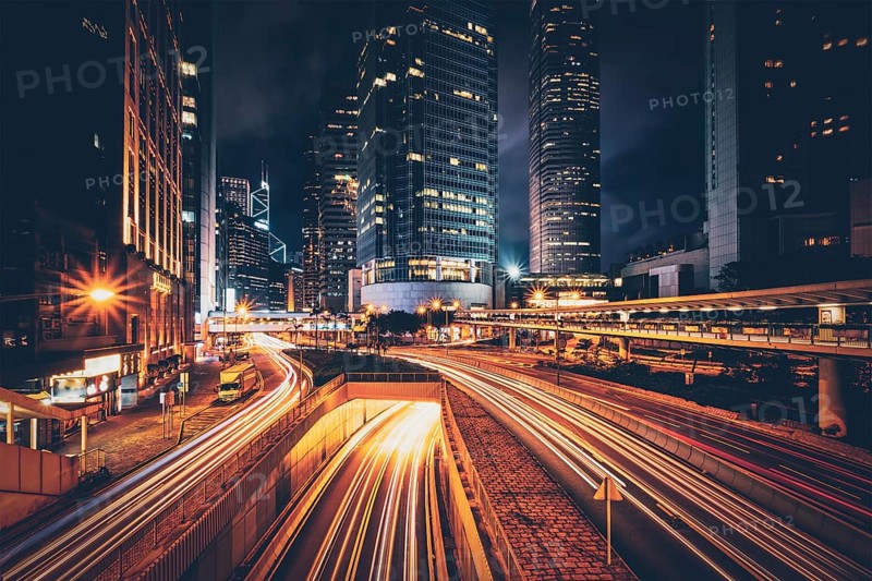 Street traffic in Hong Kong at night. Office skyscraper buildings and busy traffic on highway road with blurred cars light trails. Hong Kong
