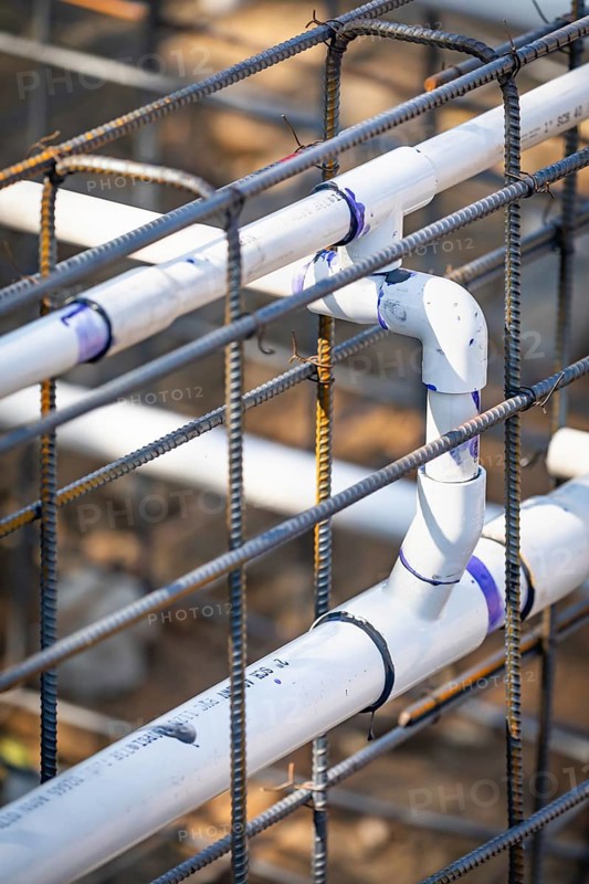 Newly installed PVC plumbing pipes and steel rebar configuration at construction site