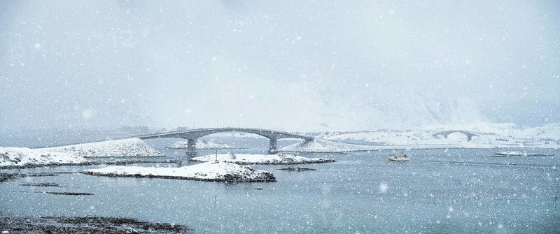 Fredvang bridges in heavy snowfall in winter with fishing ship. Lofoten islands