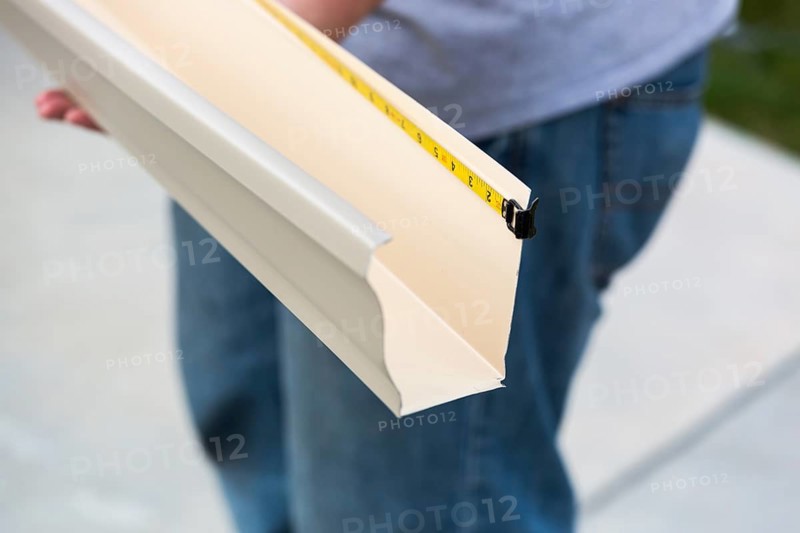 Worker measuring an aluminum rain gutter feeding through seamless shaping machine
