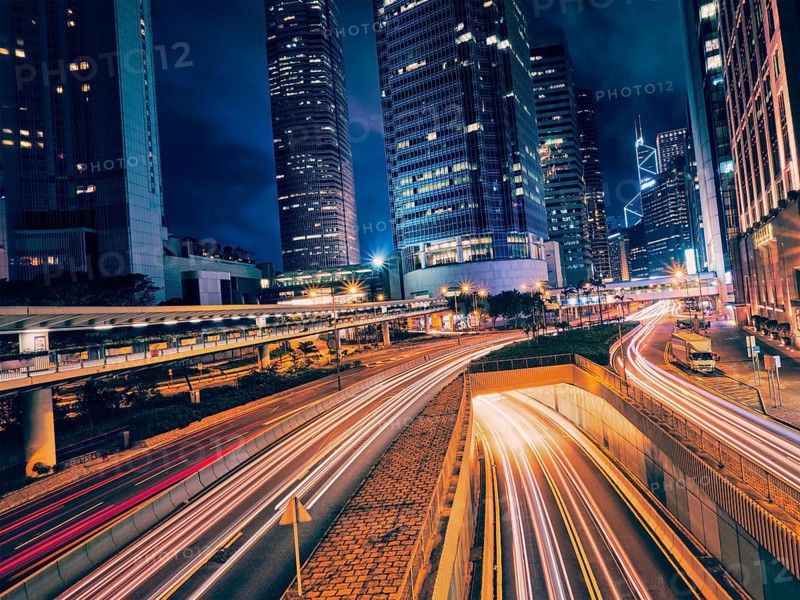 Street traffic in Hong Kong at night. Office skyscraper buildings and busy traffic on highway road with blurred cars light trails. Hong Kong