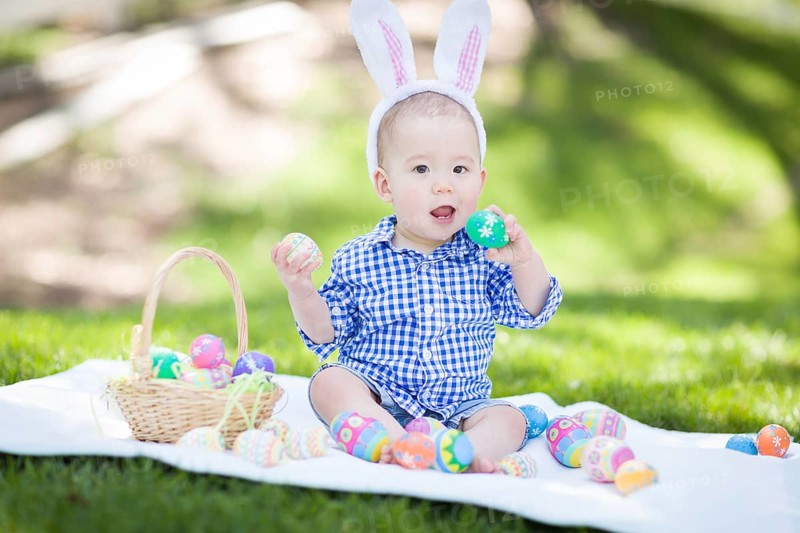 mixed-race chinese and caucasian baby boy outside wearing rabbit ears playing with easter eggs