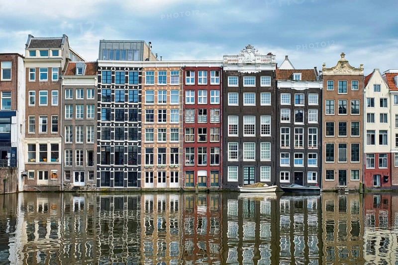 Row of typical houses and boat on Amsterdam canal Damrak with reflection. Amsterdam