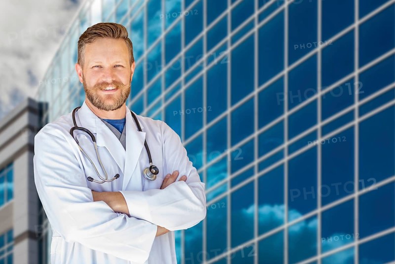 Handsome young adult male doctor with beard in front of hospital building