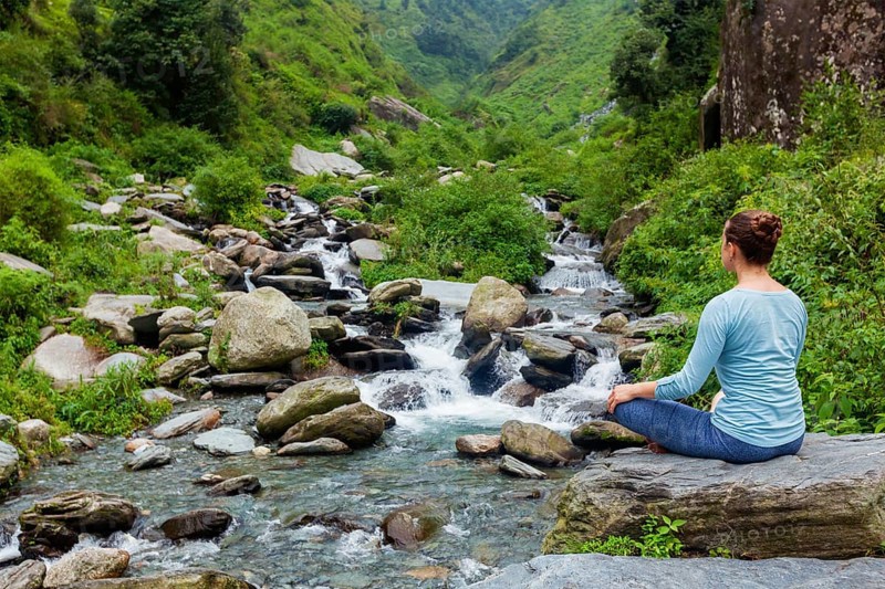 Woman in Hatha yoga asana Padmasana outdoors at tropical waterfall