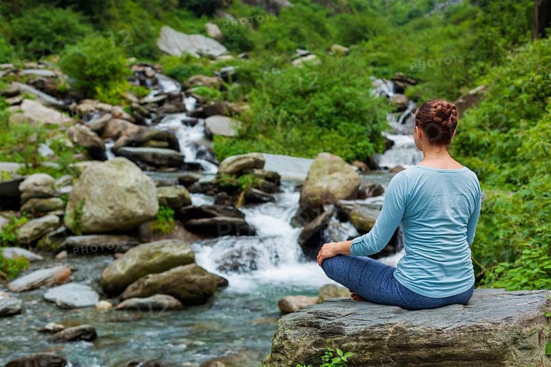 Woman in Hatha yoga asana Padmasana outdoors at tropical waterfall