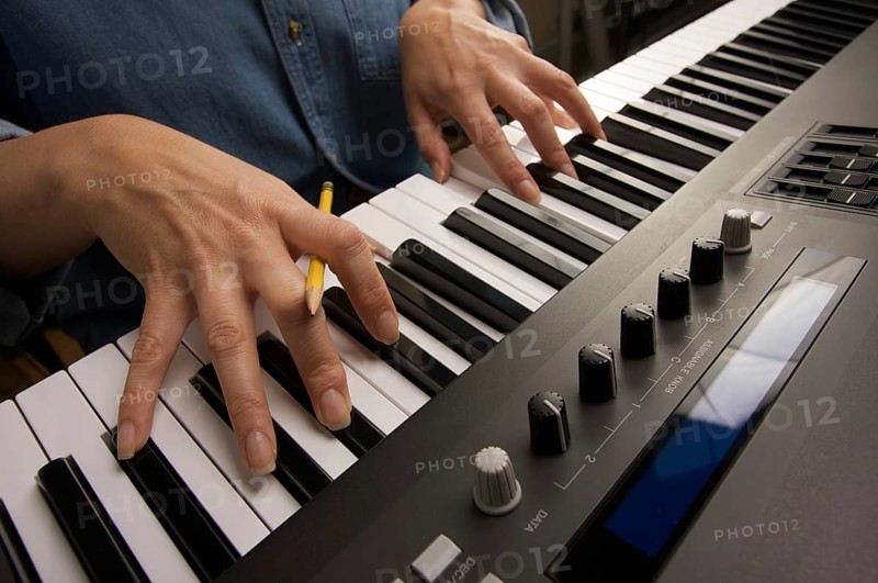 Woman's fingers with pencil on digital piano keys