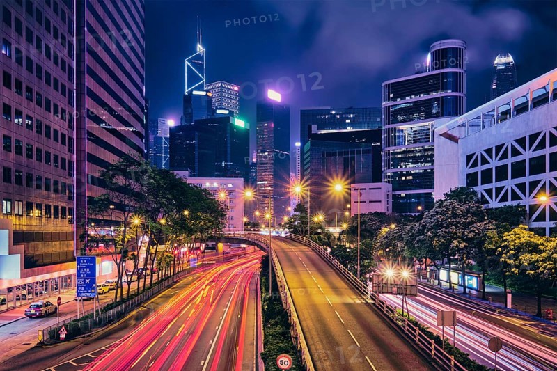 Street traffic in Hong Kong at night. Office skyscraper buildings and busy traffic on highway road with blurred cars light trails. Hong Kong