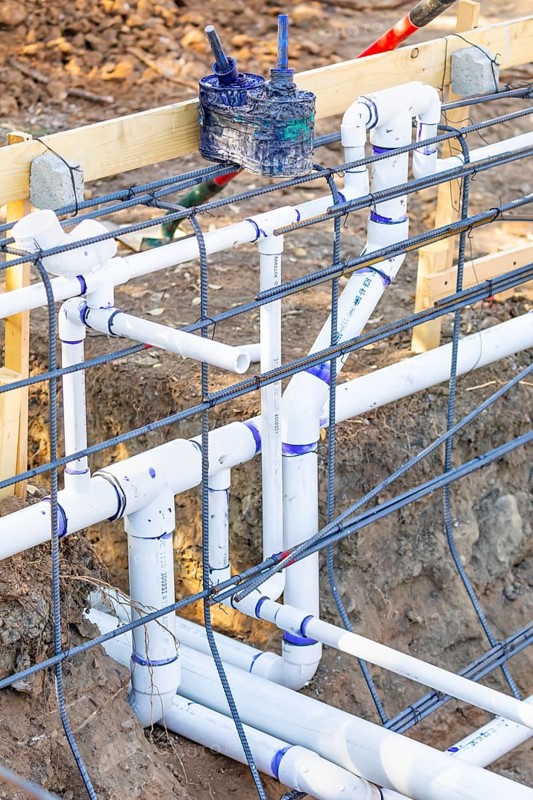 Newly installed PVC plumbing pipes and steel rebar configuration at construction site