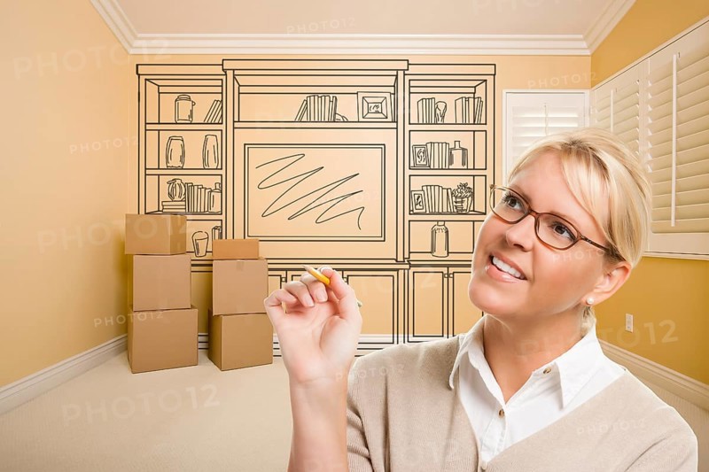 Female holding pencil in room with moving boxes and drawing of entertainment unit on wall