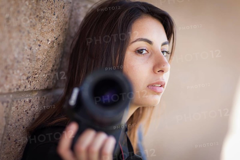 Young adult ethnic female photographer against wall holding camera