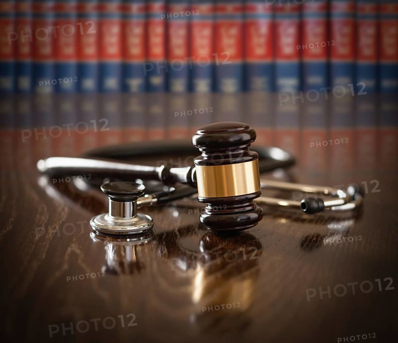 Gavel and stethoscope on wooden table with law books in background