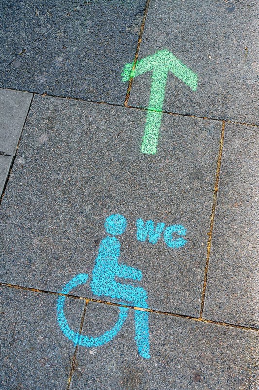 A green arrow with a blue pictogram for a wheelchair-accessible toilet points the way to a disabled toilet on the floor of the pedestrian zone