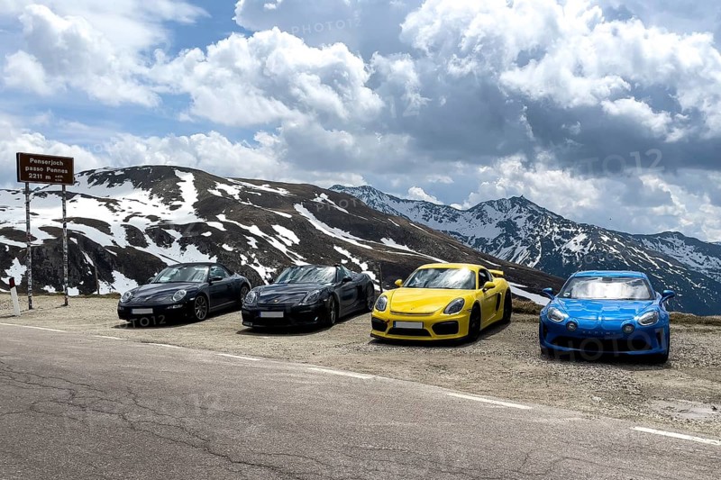 Porsche sports car and Renault Alpine standing at the top of mountain pass in Alps