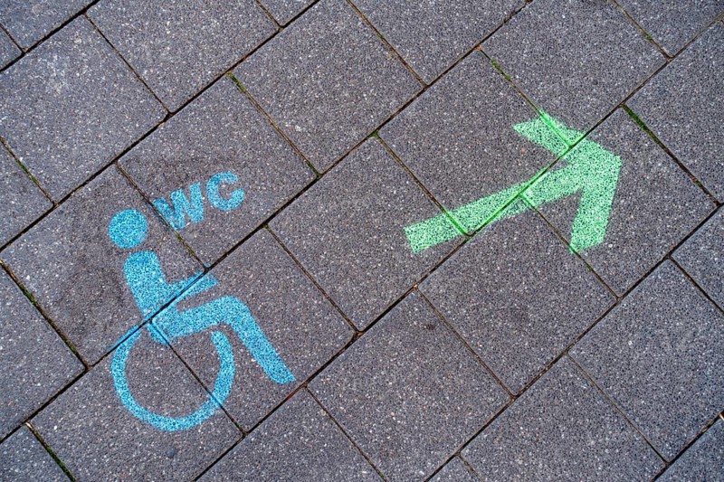 A green arrow with a blue pictogram for a wheelchair-accessible toilet points the way to a disabled toilet on the floor of the pedestrian zone