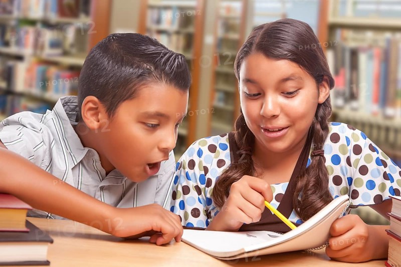 Hispanic boy and girl having fun studying together in the library