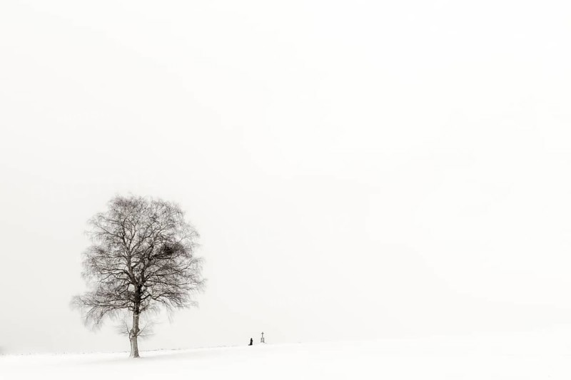 Einsame Frau knieend an Marterl mit Baum in Winterlandschaft