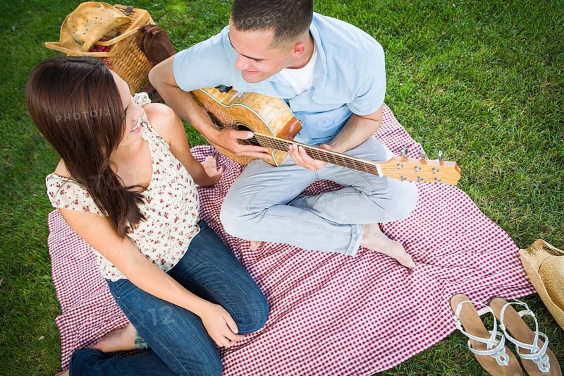 Young adult man playing guitar for his girlfriend in the park