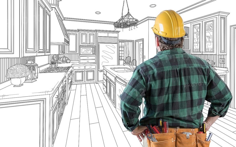 Male contractor with hard hat and tool belt looking at custom kitchen drawing on white