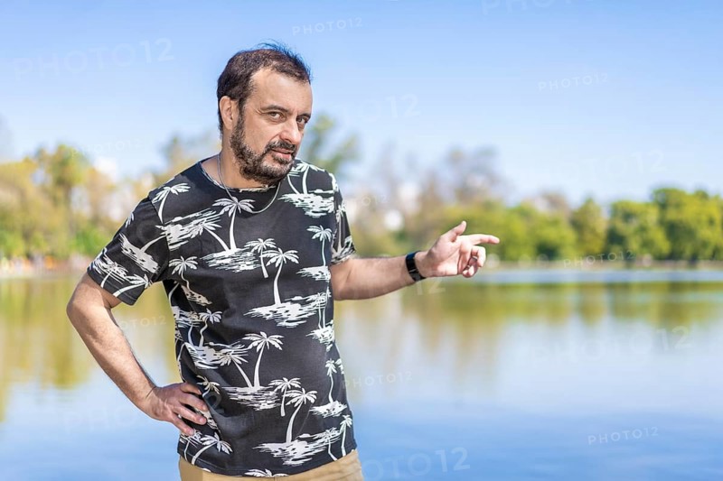 Bearded mature man in a lake looking at the camera with one arm akimbo and the other pointing to the side. Copy space