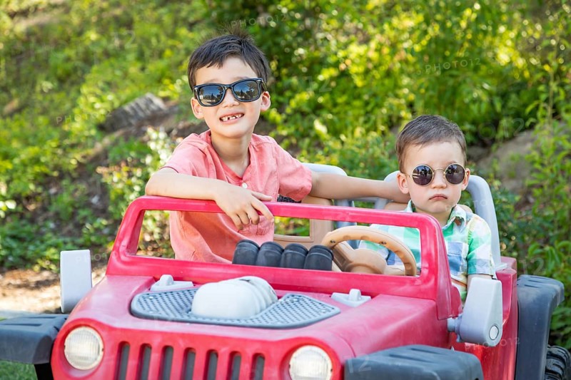 Young mixed-race chinese and caucasian brothers wearing sunglasses playing in toy car