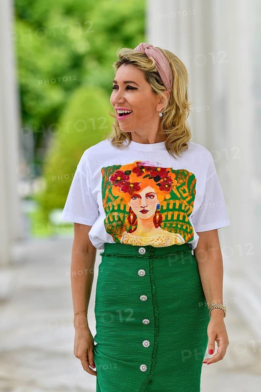 Portrait in einem Park einer huebschen Dame in ihren vierziger Jahren mit langen blonden Haaren. Sie geht auf die Kamera zu und blickt mit ueberraschte Blick zu Seite. Ein gruener langer Rock mit bedrucktem Shirt ergibt ein elegantes Outfit
