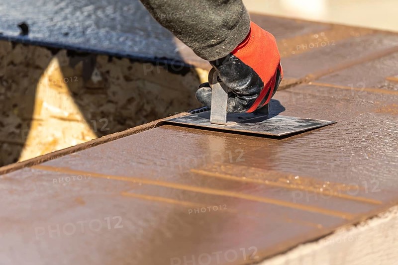 Construction worker using hand groover on wet cement forming coping around new pool