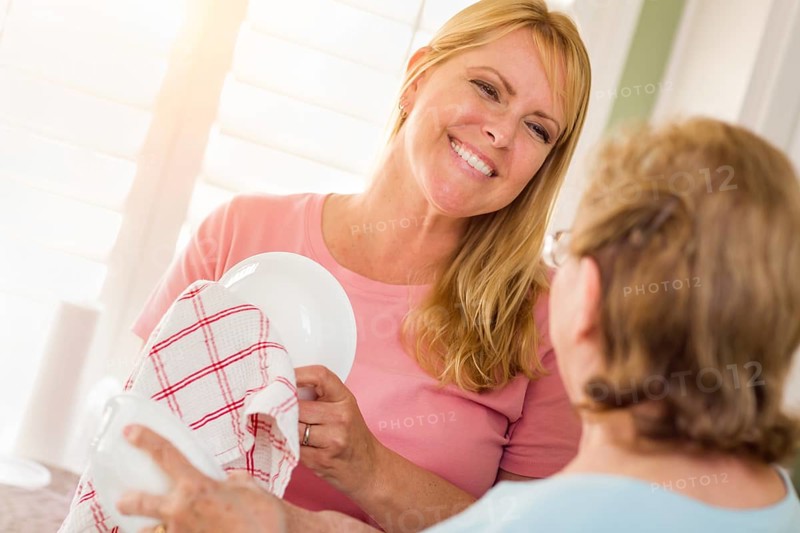 Senior adult woman and young daughter talking at sink in kitchen
