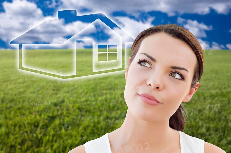 Contemplative woman in grass field looking up and over to the side with ghosted house figure behind