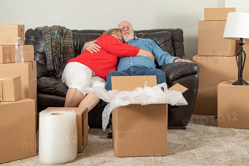 Affectionate tired senior adult couple resting on couch surrounded by moving boxes