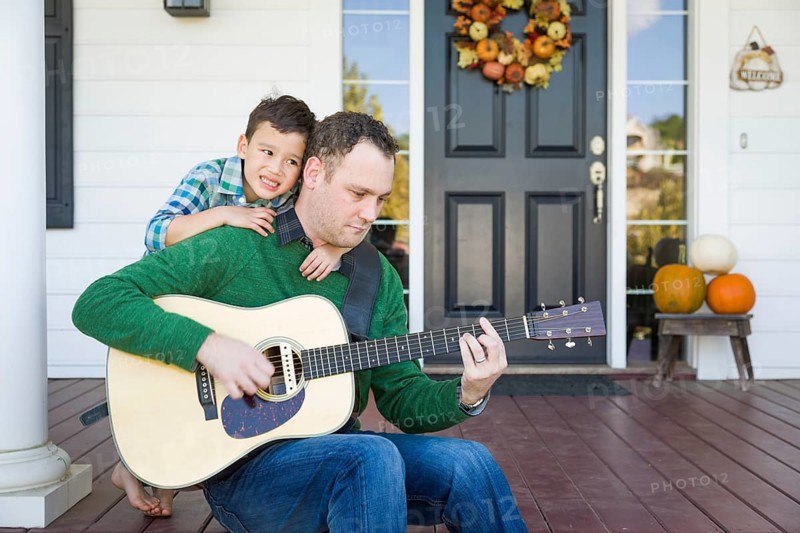 Young mixed-race chinese and caucasian son singing songs and playing guitar with father